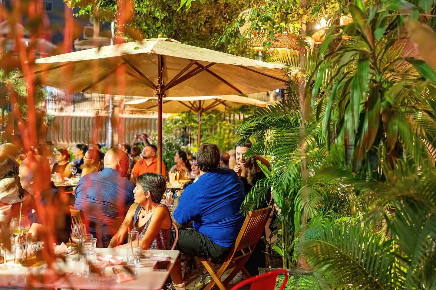 Guests dining under an umbrella at Bellini, warm lanterns glowing through the garden