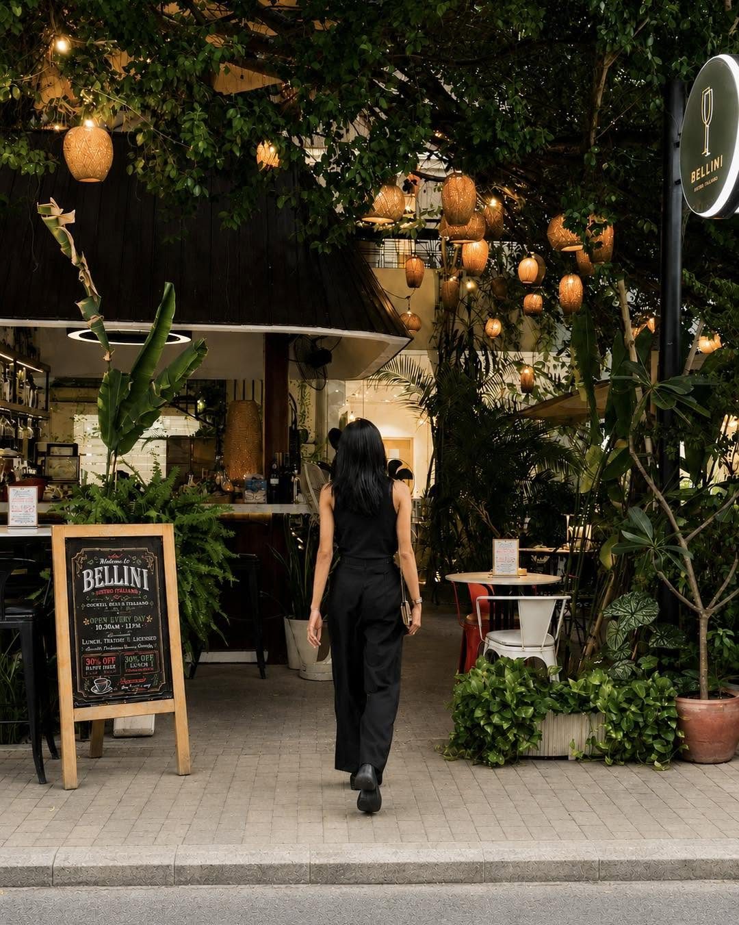 Guest walking into Bellini Bistro Italiano past the chalkboard sign, lanterns glowing in the garden, Phnom Penh